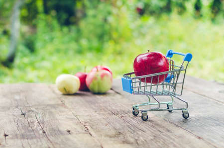 Small shopping trolley with ripe red apple on old wooden table.