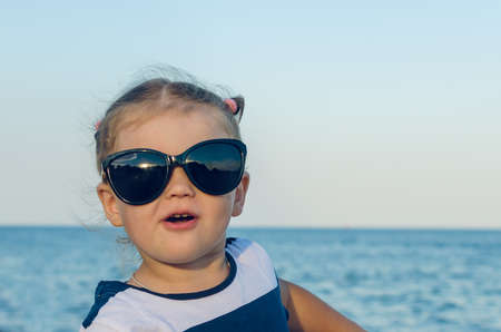 Portrait of a little girl in sunglasses by the sea.の写真素材