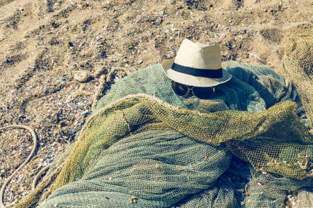 Hat and sunglasses lie on a fishing net on a sandy seashore.の写真素材