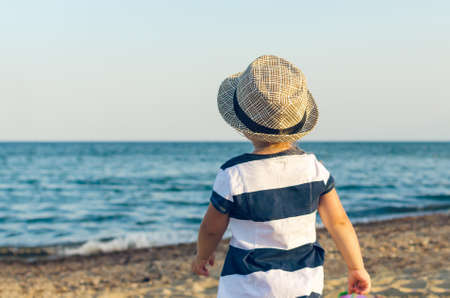 Little girl in a hat walks along the seashore.の写真素材