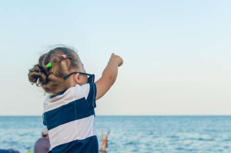 A little girl in sunglasses shows on something with her hand.の写真素材