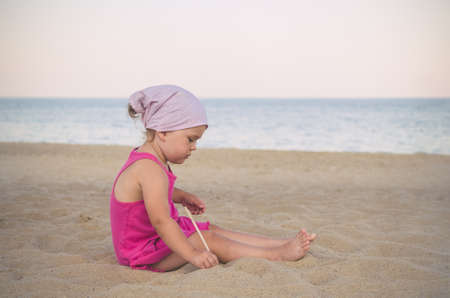 Little girl in kerchief plays in the sand on the sea in summer.の写真素材
