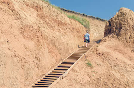Young man in a hat rises up the wooden stairs.
