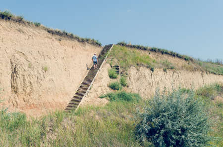 Young man in a hat rises up the wooden stairs.