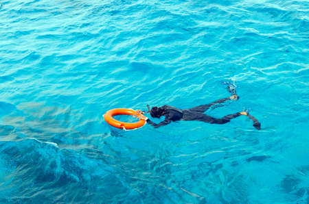 A young man in a diving suit and flippers swims in the sea holding the lifebuoy.の写真素材