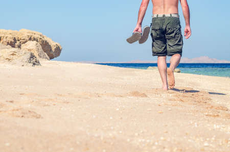 Barefoot man walks along the sandy sea coast.の写真素材