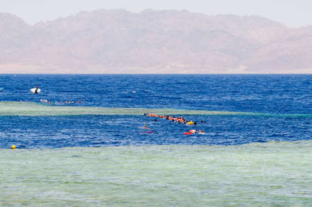 People in masks for snorkeling swim in the pool of a coral reef. Tourist lifestyle, water sports.の写真素材