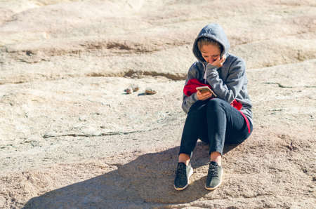 Sinai Peninsula, Egypt, May 9, 2019: A girl sits on stones and uses her mobile phone.の写真素材