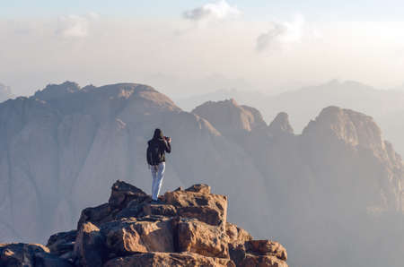 Male tourist photographs the landscape in the mountains on a mobile phone.の写真素材