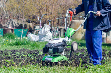 A man plows the land with a cultivator in a spring garden.