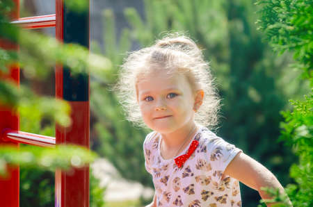 Portrait of a little girl exercising on a horizontal bar on a sports field in the sunlight.