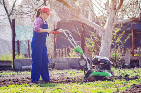Young girl plows the land with a cultivator in spring garden.の写真素材