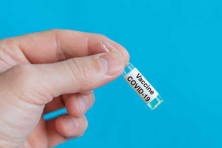 Ampule in hand with covid-19 coronavirus vaccine on a blue background.