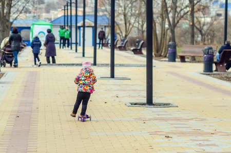 Little girl riding a scooter in the city alley.の写真素材