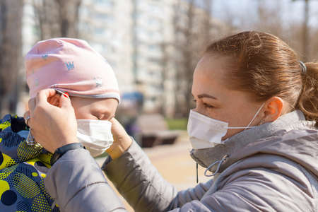 Mom helps her little daughter put on a medical protective mask. Covid-19 Coronavirus Pandemic, Virus...