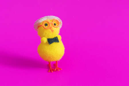 Toy chicken in glasses and hat on a pink background.