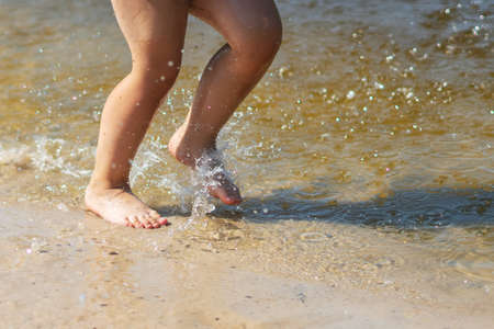 A child runs along the river bank splashing water with his feet.