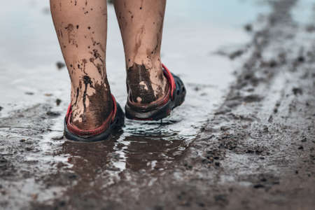 Children's feet walking in a muddy puddle after the rain.の写真素材