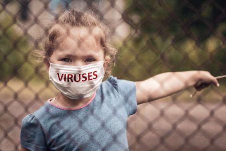 A child in a medical mask with the inscription Viruses behind a fence in the street. Pandemic coronavirus Covid-19, virus protection.の写真素材