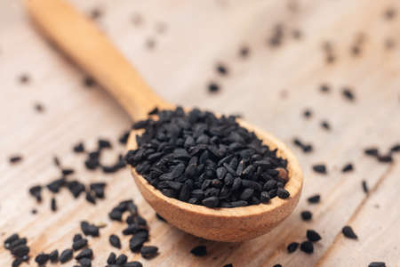 Black cumin seeds on wooden spoon on wooden background.