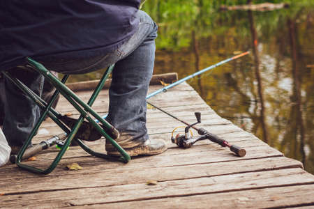 A fisherman sits on an old wooden bridge and catches fish.の写真素材