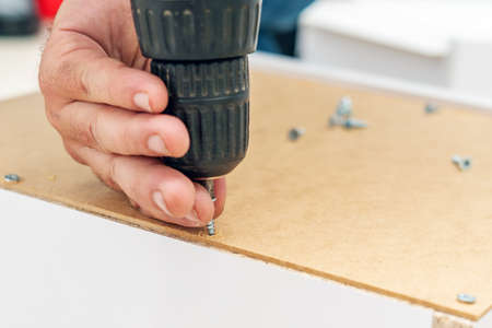 Assembly of furniture, the carpenter screws a self-tapping screw into a drawer with a screwdriver.
