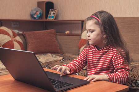 Smiling little girl using laptop for distance learning or for fun.