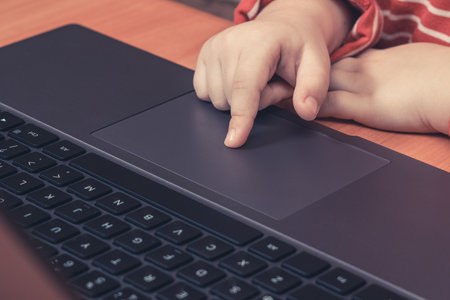 Kid hands on laptop touchpad, child learns and plays on computer.