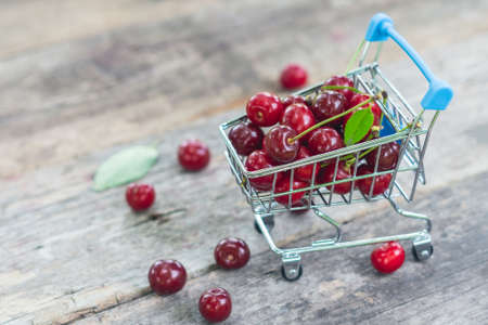Fresh ripe cherries in a shopping trolley on wooden background.の写真素材