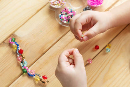 The child makes jewelry with his own hands, stringing colorful beads on a thread.の写真素材