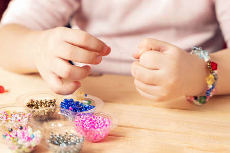 The child makes jewelry with his own hands, stringing colorful beads on a thread.の写真素材