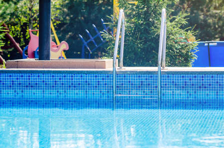 Steel ladder in a swimming pool with blue water on a sunny day.
