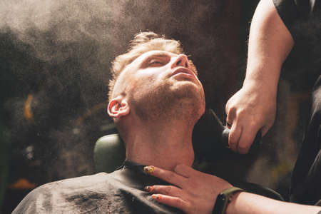 Hands of a hairdresser girl apply talcum powder on a client's face with a brush in a barbershop.