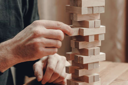 The hands of a man playing a board game builds a tower from wooden blocks.