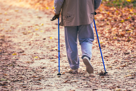 Nordic walking, retirement age woman exercising in autumn city park.
