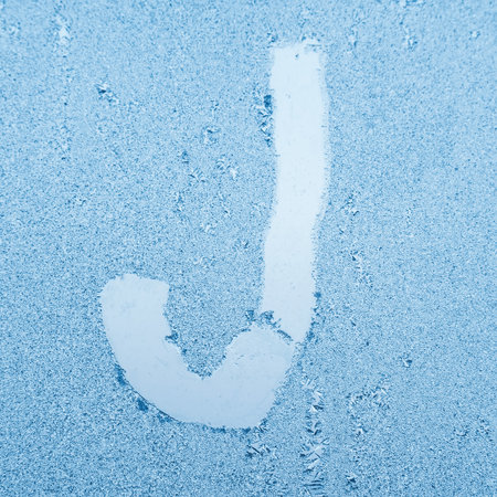 The letter J written on glass with frost in the frost in winter, close up.の写真素材