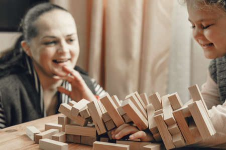 Mom and daughter play a board game, build a tower from wooden blocks.の写真素材