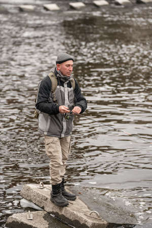 Man fishing on the river. Fisherman with a fishing rod on the background of water in cloudy weather.