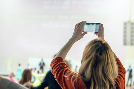 Woman photographing an event using a smartphone, view from the back.の写真素材