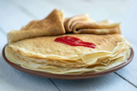Crepes, thin pancakes on a plate on a white wooden table.