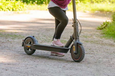 Little girl rides an electric scooter on a dirt road in the park.の写真素材
