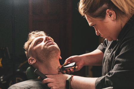 Bearded man in a barbershop, hands of a hairdresser with a beard clipper, close up.の写真素材