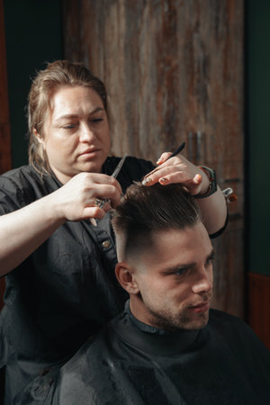 Girl hairdresser doing hairstyle and styling with scissors and comb to a young man.の写真素材