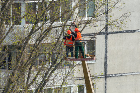 Workers in the city cut trees with a chainsaw while standing on a crane lift.の写真素材