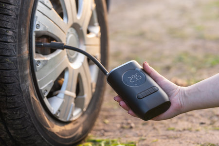A woman's hand holds a wireless portable air pump for inflating car tires.の写真素材