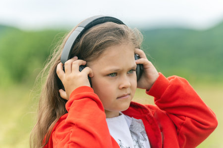 Cute little girl in modern wireless headphones enjoy music outdoors.の写真素材
