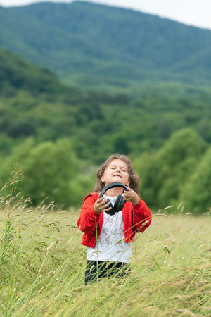 Cute little girl in modern wireless headphones enjoy music outdoors.の写真素材