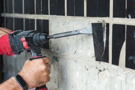 Builder with a puncher dismantles old tiles from a concrete wall.の写真素材