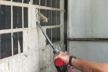 Builder with a puncher dismantles old tiles from a concrete wall.の写真素材