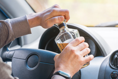 The driver is sitting behind the wheel and holding a bottle of alcoholic drink. Breaking the law and...